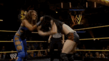 a woman in a blue top is standing in a wrestling ring with a w logo on the ropes