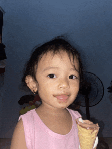 a little girl in a pink tank top is eating an ice cream cone with chocolate on her face
