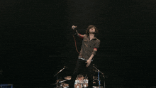 a man singing into a microphone on a stage with a drum set in the background