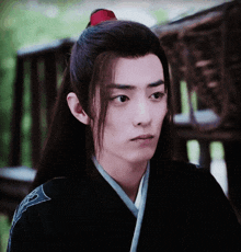 a young man with long hair and a red flower in his hair looks at the camera