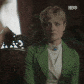 a woman in a green jacket is sitting on a couch with hbo written on the bottom