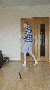 a man in a plaid shirt and shorts is walking on a wooden floor
