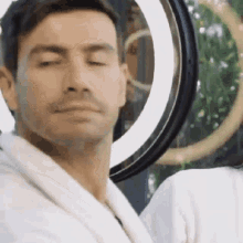 a man wearing a bathrobe is looking at himself in a mirror .