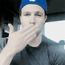 a man wearing a blue hat and a black shirt is blowing a kiss