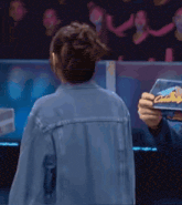 a man in a denim jacket is holding a piece of paper that says ' a ' on it