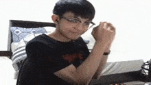 a young man wearing glasses and ear buds is sitting in front of a bed .