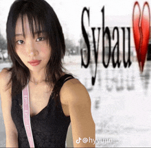 a woman in a black tank top is standing in front of a sign that says sybeau