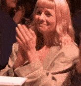 a woman is clapping her hands while sitting in a crowd