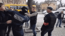 a group of men are standing on a sidewalk and one of them is wearing a blue jacket with the word militia on it .