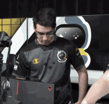a man wearing glasses and a champion shirt stands in front of a computer monitor