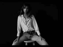 a woman in a white shirt sits on a wooden stool