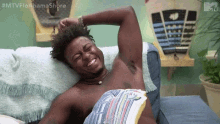 a shirtless man is laying on a couch with his arms outstretched and smiling .