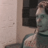 a man wearing a red sox shirt is sitting in a room with a door in the background .