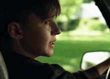 a close up of a person driving a car with a green background