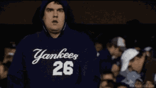 a man wearing a yankees 26 hoodie stands in a crowd