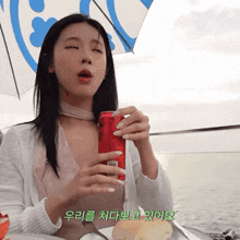 a woman drinking from a red can with foreign writing on the bottom
