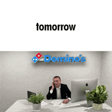 a man sits at a desk with a domino 's sign above him