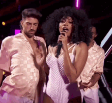 a woman is singing into a microphone while two men are dancing behind her