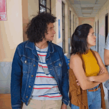 a man in a denim jacket stands next to a woman in a yellow top in a hallway