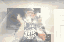 a man wearing a shirt that says tfr is standing in front of a television