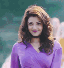 a woman in a purple top and purple lipstick smiles