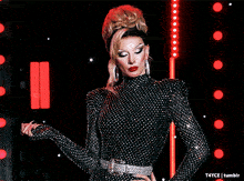 a woman in a black and silver polka dot dress is standing in front of red lights and a tumblr logo