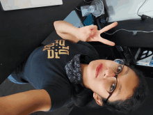 a woman wearing glasses and a black shirt that says dig is giving a peace sign