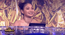 a woman is sitting at a table with a computer in front of a gold background .