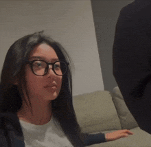 a woman wearing glasses is sitting on a couch and looking at the camera