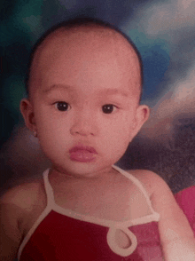 a baby is wearing a red tank top with a white ribbon around the neck