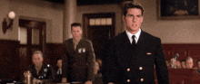 a man in a suit and tie stands in front of a group of men in military uniforms