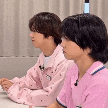 two young men wearing pink shirts are sitting at a table