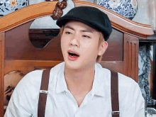 a man wearing a hat and suspenders is sitting on a wooden chair