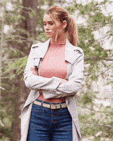 a woman with her arms crossed wearing a pink turtleneck and blue jeans