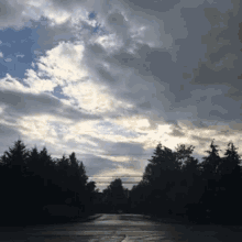 a cloudy sky with a few trees in the foreground