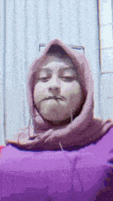 a woman wearing a purple hoodie and a pink hijab is making a face