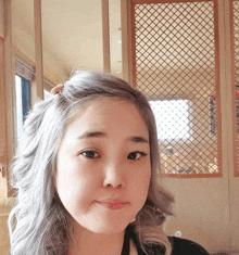 a woman with gray hair stands in front of a wooden fence