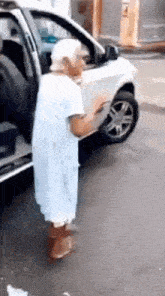 an elderly woman in a hospital gown is dancing in front of a car .