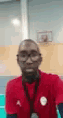 a man with glasses and a red shirt is standing in front of a basketball hoop .