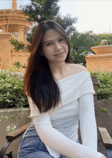 a woman in a white off the shoulder top sits on a bench in front of a fountain