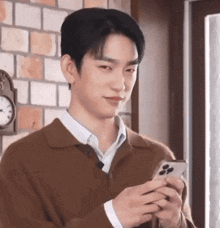 a young man in a brown sweater is holding a cell phone .