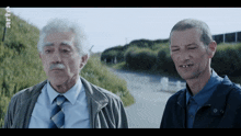 two men are standing next to each other on a road with the letters rtl on the bottom left