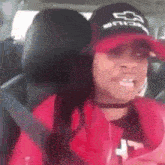 a woman wearing a red jacket and a black hat is sitting in a car with her seat belt on .