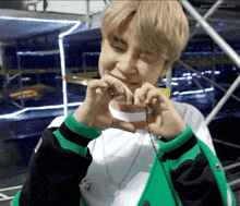 a young man wearing a green jacket is making a heart shape with his hands