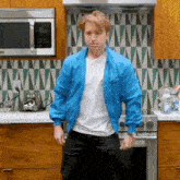 a man in a blue jacket stands in a kitchen
