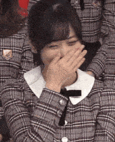 a woman in a plaid shirt is covering her mouth with her hands .