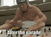 a shirtless man wearing a helmet is playing with toy soldiers with the caption " after the parade "