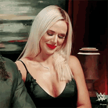 a blonde woman wearing a black tank top and red lipstick is smiling and looking down .