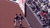 a couple of baseball players are walking on a field while a crowd watches .