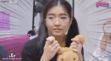 a woman wearing glasses is holding a teddy bear and a cupcake in her hands .